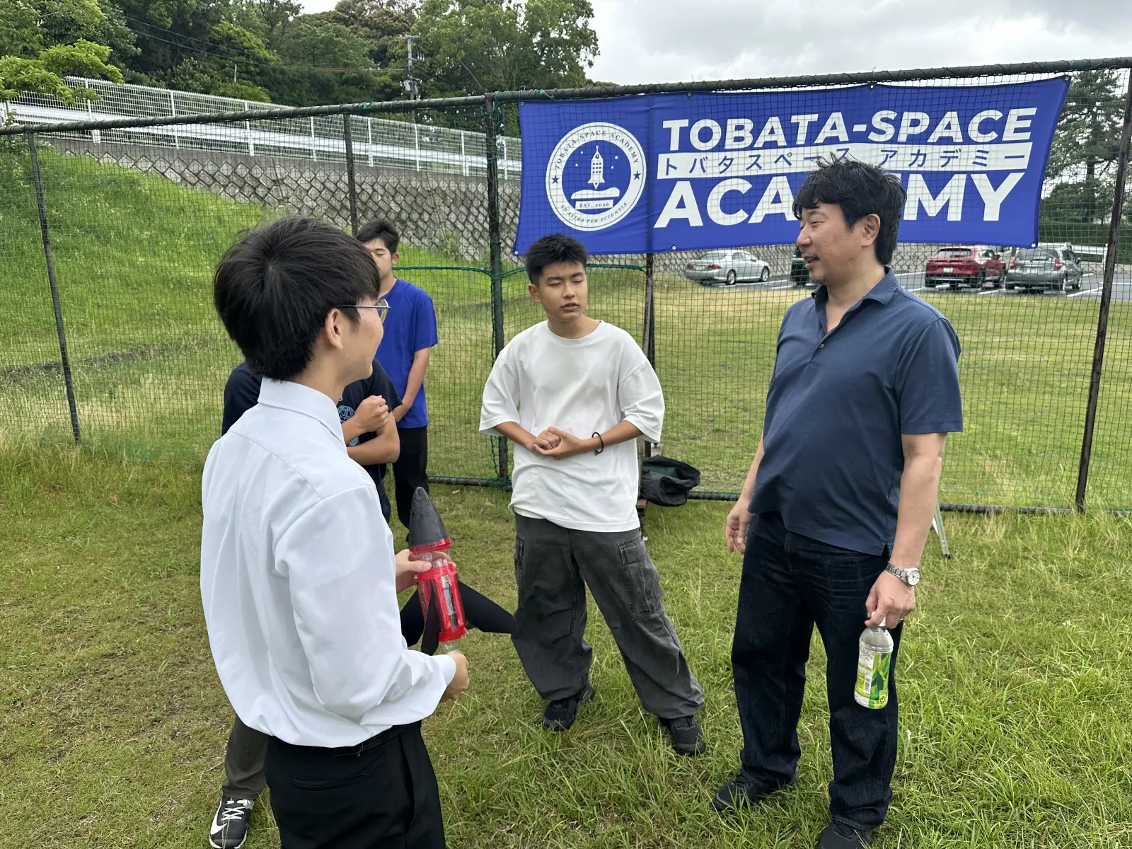 グラウンドで前田先生・布施先生を囲んで質問するアカデミー生たち