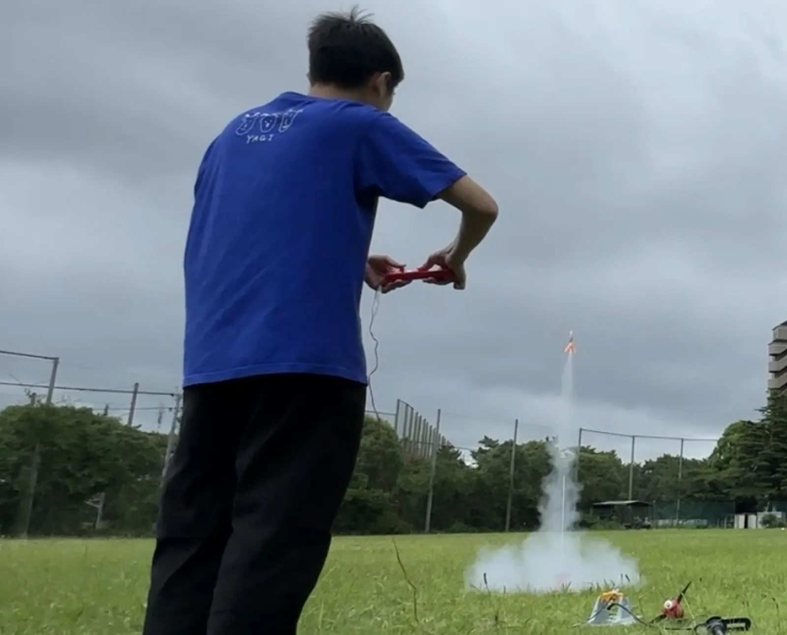 点火コントローラーを握り、白煙を噴き上げて打ち上がるモデルロケットを見送るアカデミー生