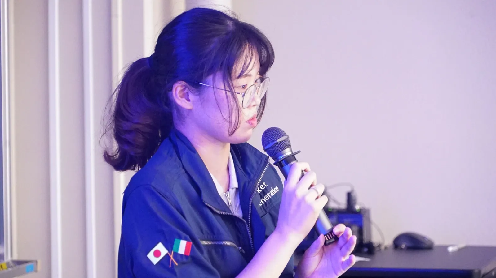 マイクを持ち、衛星プロジェクトについて説明する九州工業大学の学生
