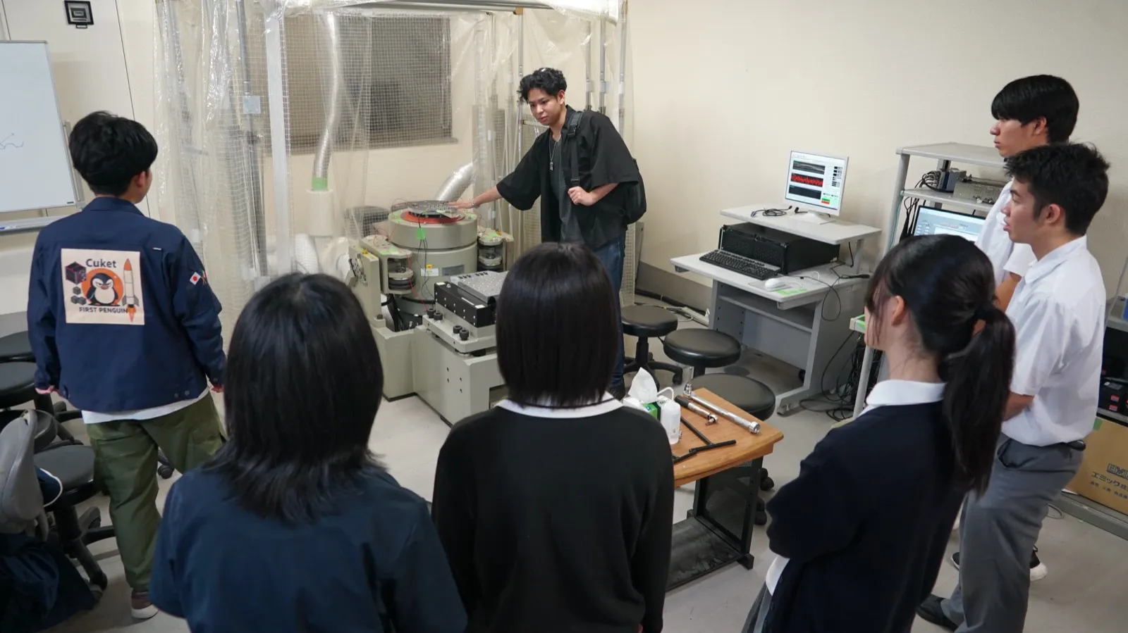 振動試験装置の前で、学生の説明を聞くアカデミー生たち